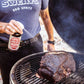 Meat Sweats Hog Wash BBQ spritz being sprayed onto pork on a smoker