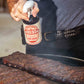 Meat Sweats Hog Wash BBQ spritz being sprayed over ribs on a smoker