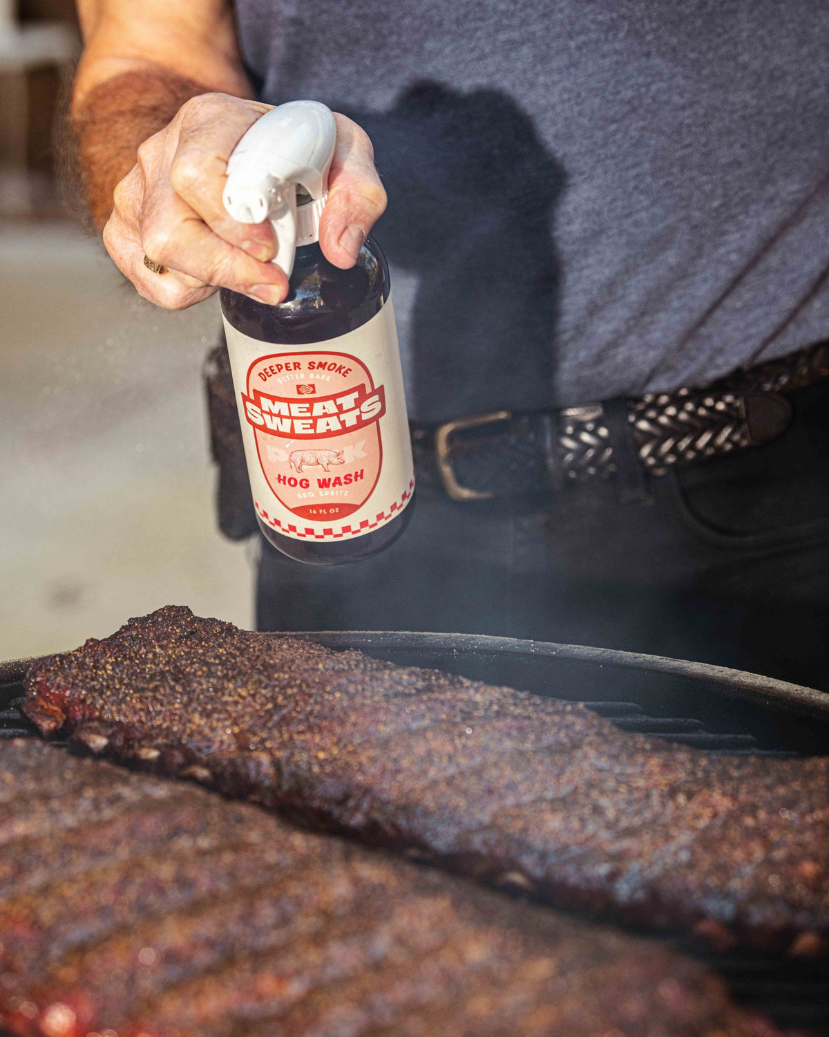 Meat Sweats Hog Wash BBQ spritz being sprayed over ribs on a smoker
